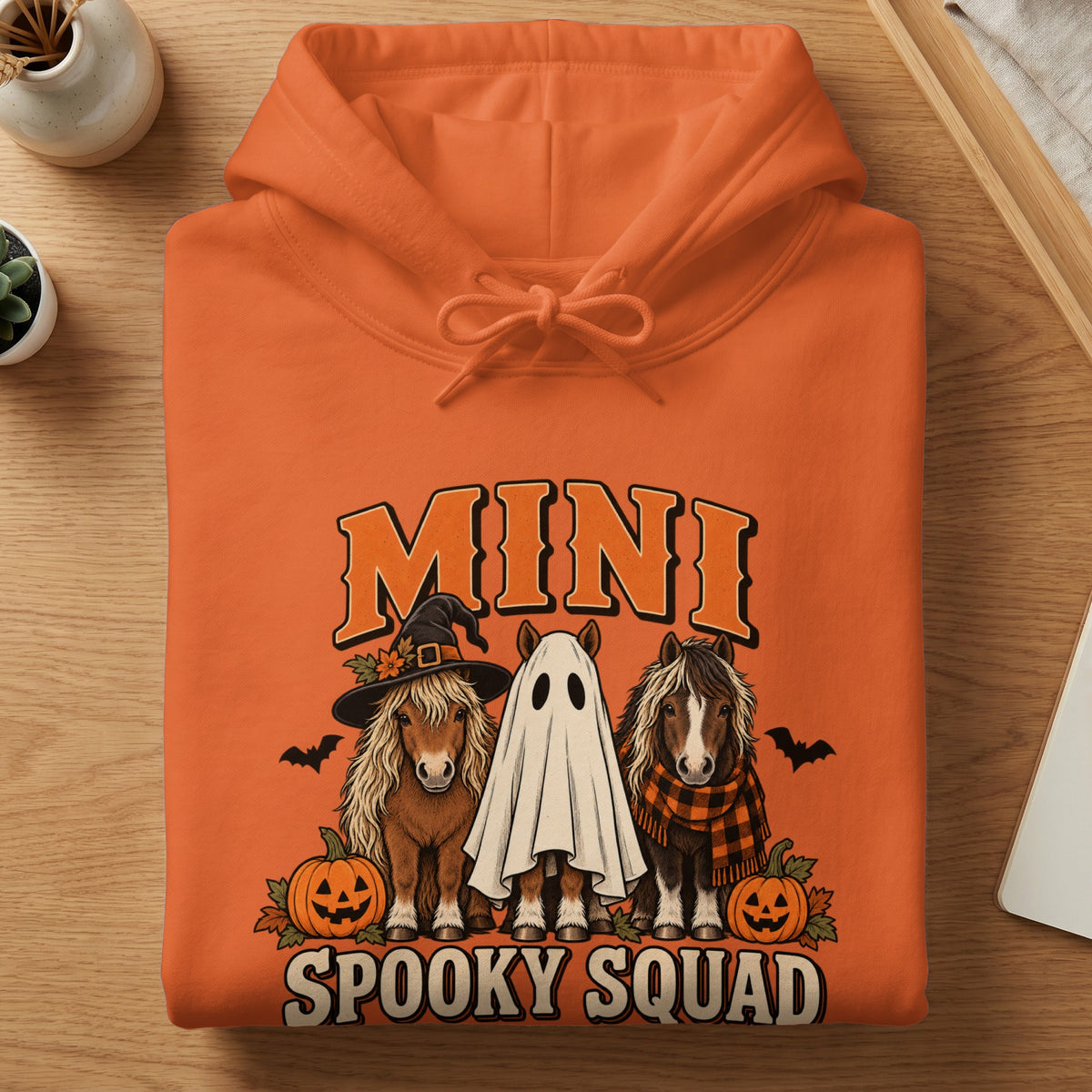 Orange hoodie with "Mini Spooky Squad" text and three horses in Halloween costumes.