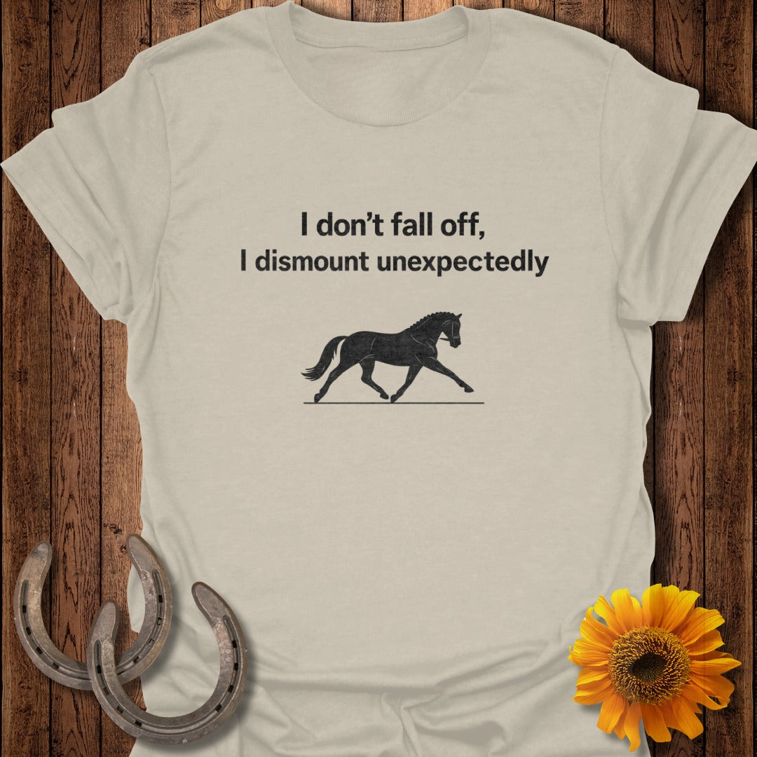 Light tan t-shirt with black text "I don't fall off, I dismount unexpectedly" and horse silhouette.