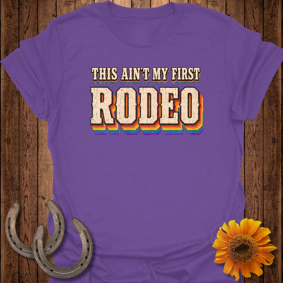 Purple t-shirt with "THIS AIN'T MY FIRST RODEO" in rainbow letters.