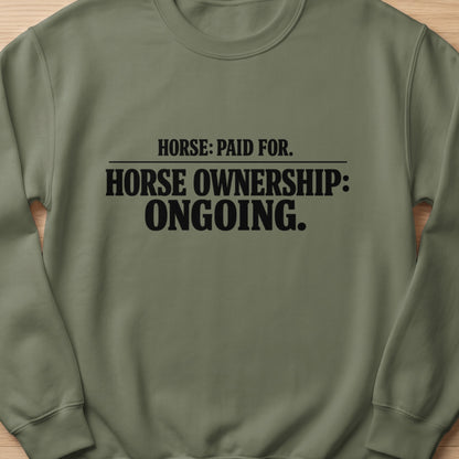 Olive green sweatshirt with black text reading "HORSE: PAID FOR. HORSE OWNERSHIP: ONGOING."