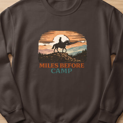Crewneck sweatshirt with "Miles Before Camp" and a cowboy on horseback at sunset graphic.