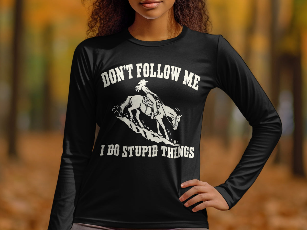 A person wearing a black long-sleeve shirt with white text reading DON'T FOLLOW ME I DO STUPID THINGS above a graphic of a person riding a horse.