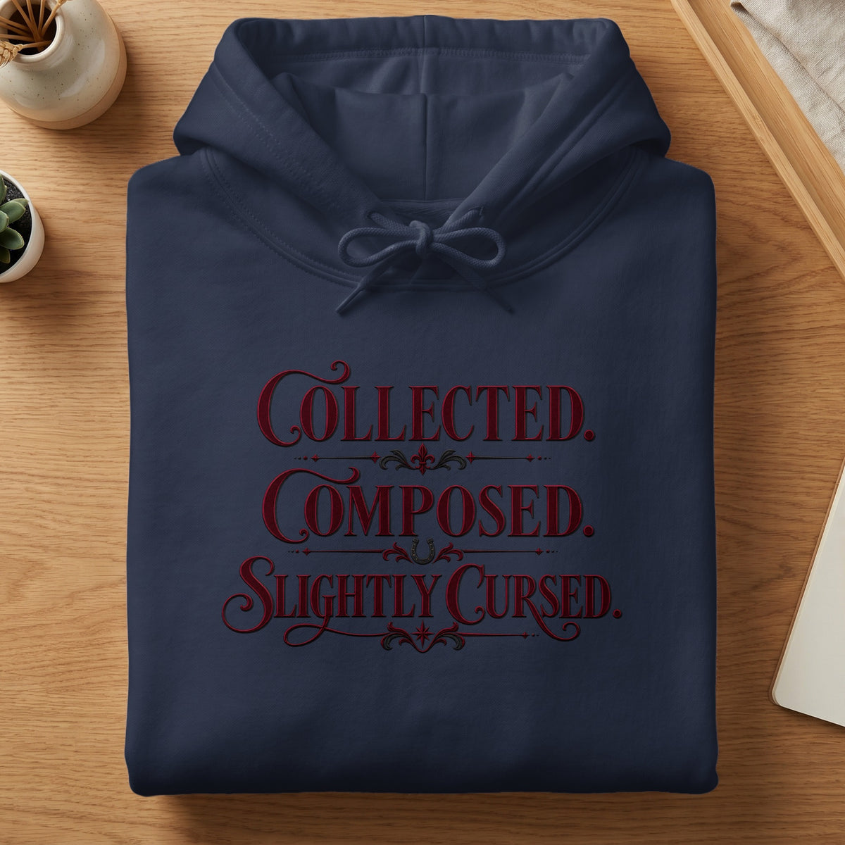 Navy hoodie with "Collected. Composed. Slightly Cursed." text in red.