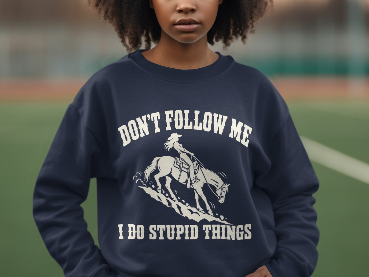 A person wears a dark blue crewneck sweatshirt featuring a white graphic of a horse and rider and the text, "DON'T FOLLOW ME I DO STUPID THINGS."