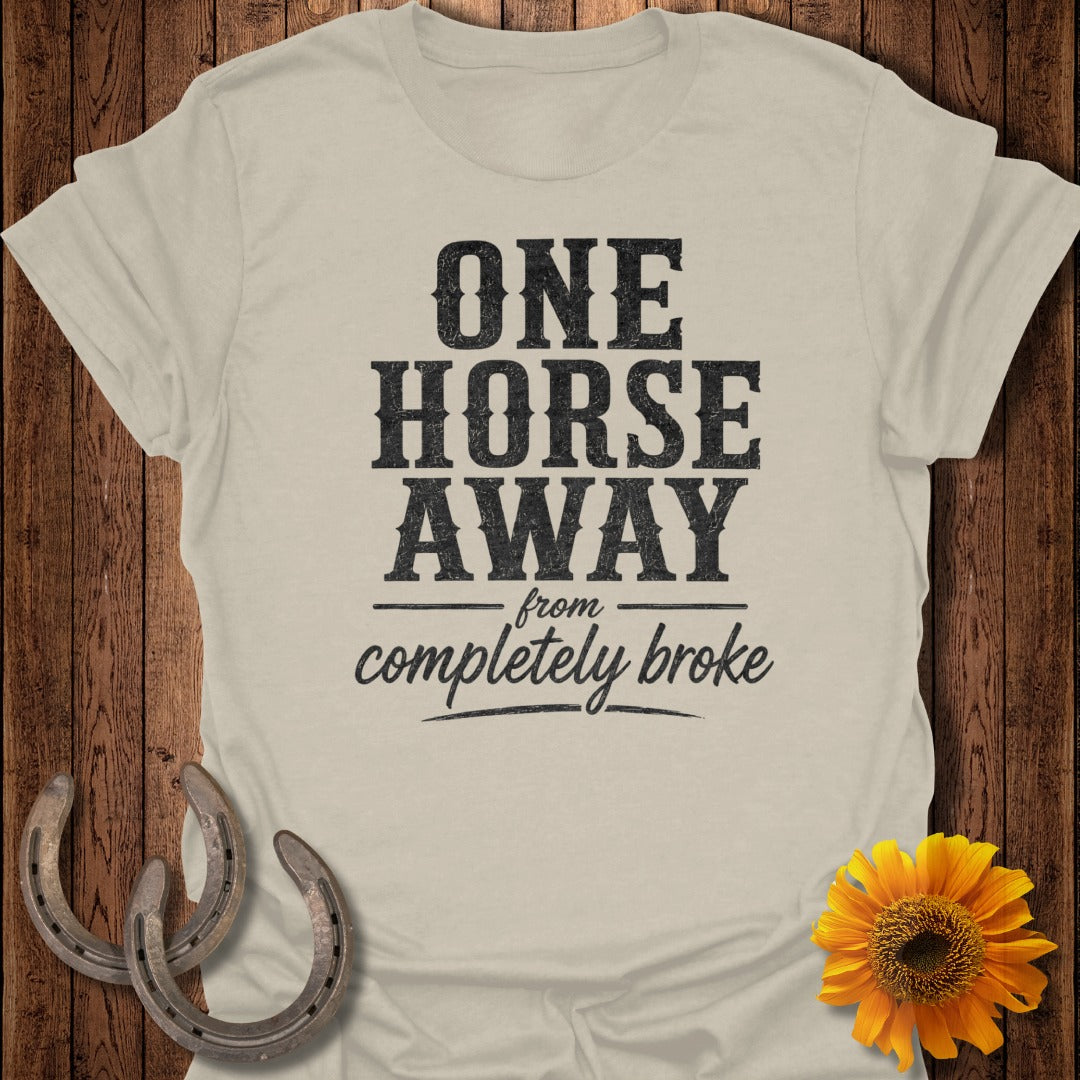 Cream t-shirt with "ONE HORSE AWAY from completely BROKE" text, horseshoes, and sunflower.