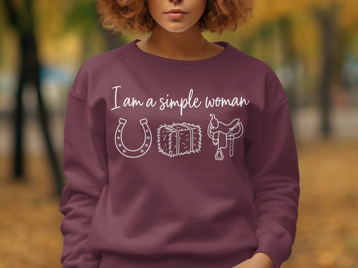 Burgundy sweatshirt with white text "I am a simple woman" and icons of a horseshoe, hay bale, and saddle.