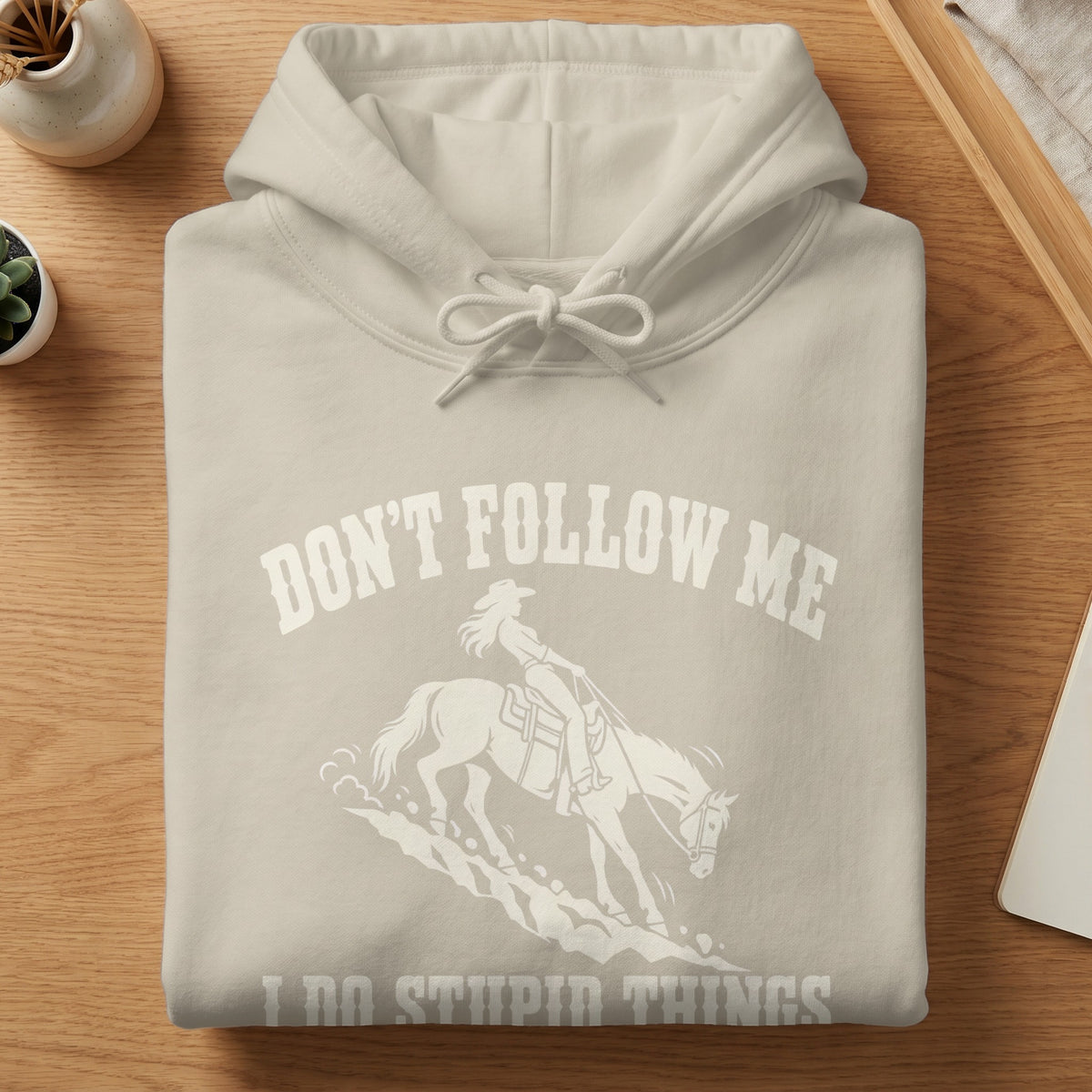 Cream-colored hoodie with a graphic of a cowgirl riding a horse and text reading Don't Follow Me I Do Stupid Things.