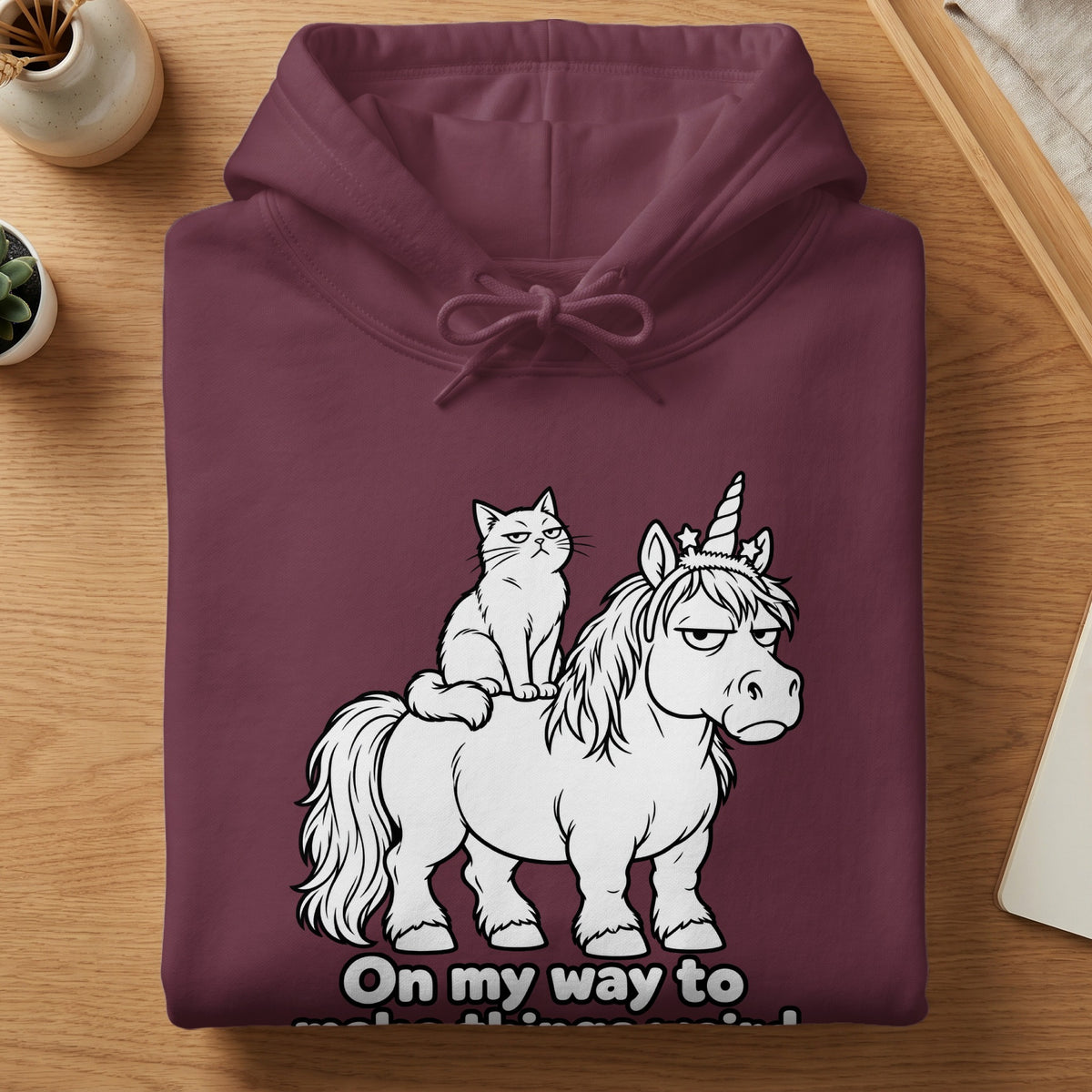 Maroon hoodie with a white cartoon cat riding a grumpy unicorn.