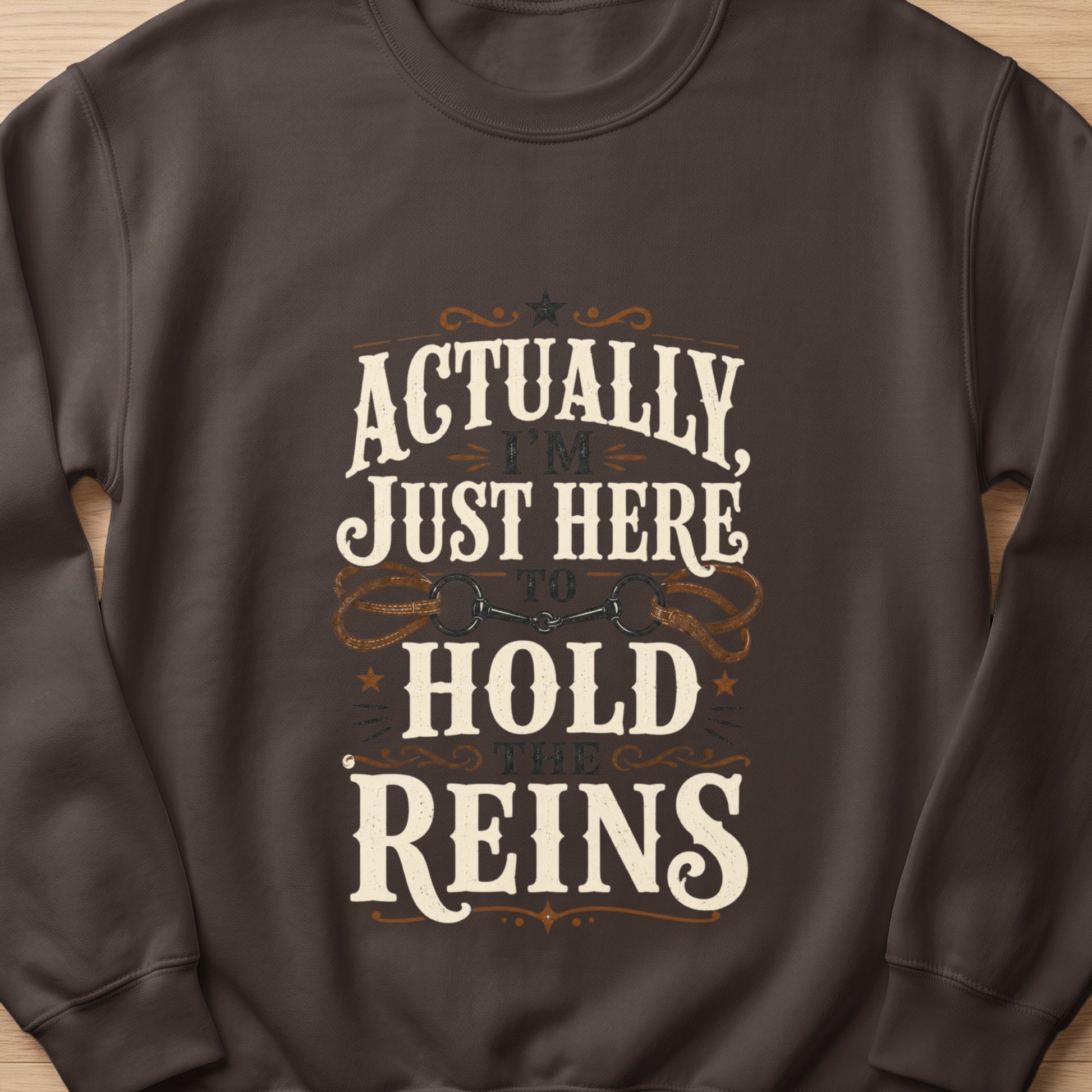 Dark brown sweatshirt with "Actually I'm Just Here To Hold The Reins" graphic.