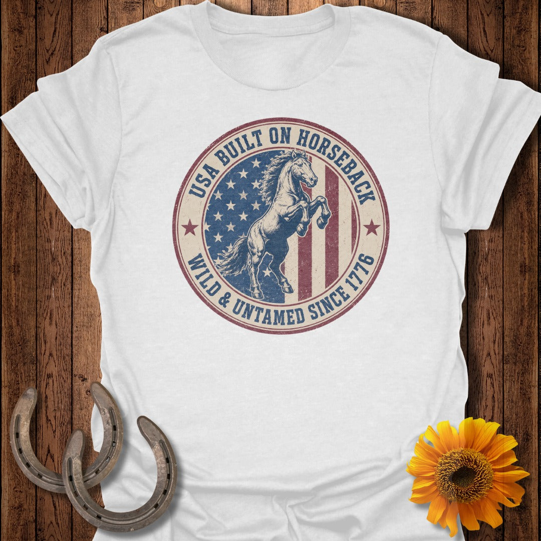 White t-shirt with circular graphic of a rearing horse and text "USA Built On Horseback Wild & Untamed Since 1776".