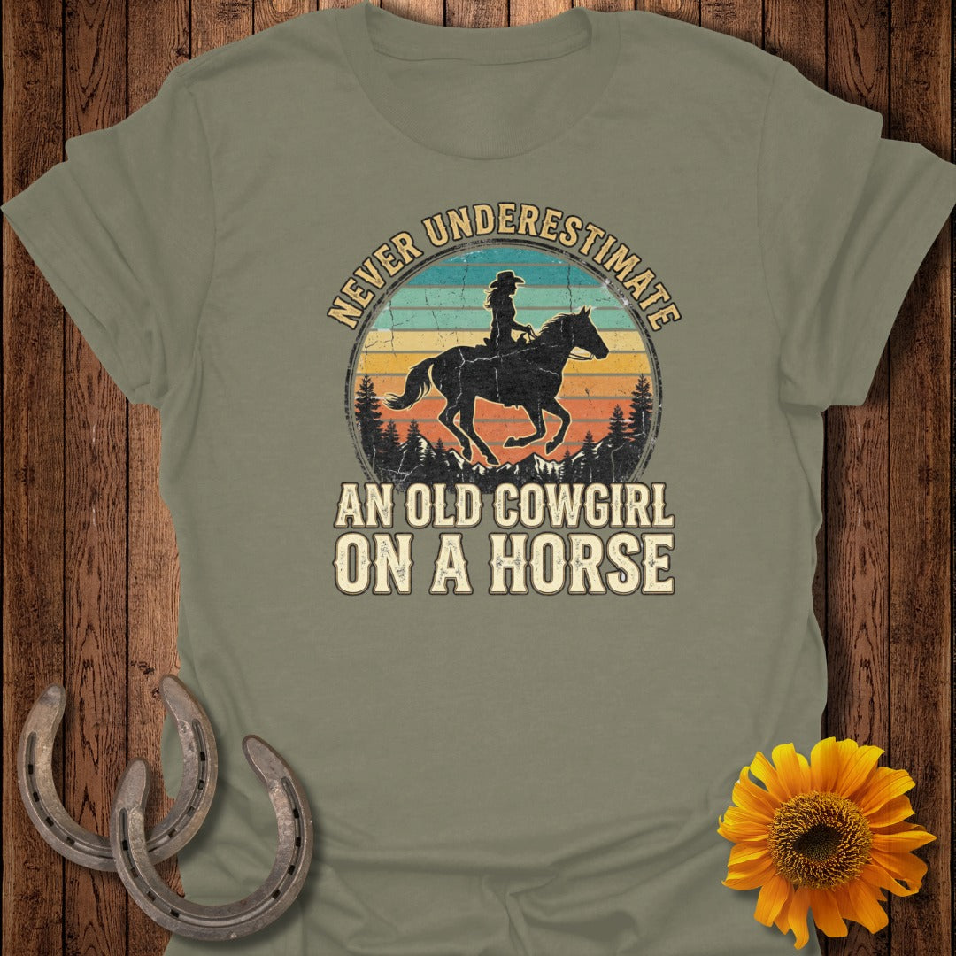 T-shirt with vintage sunset graphic: "Never underestimate an old cowgirl on a horse."