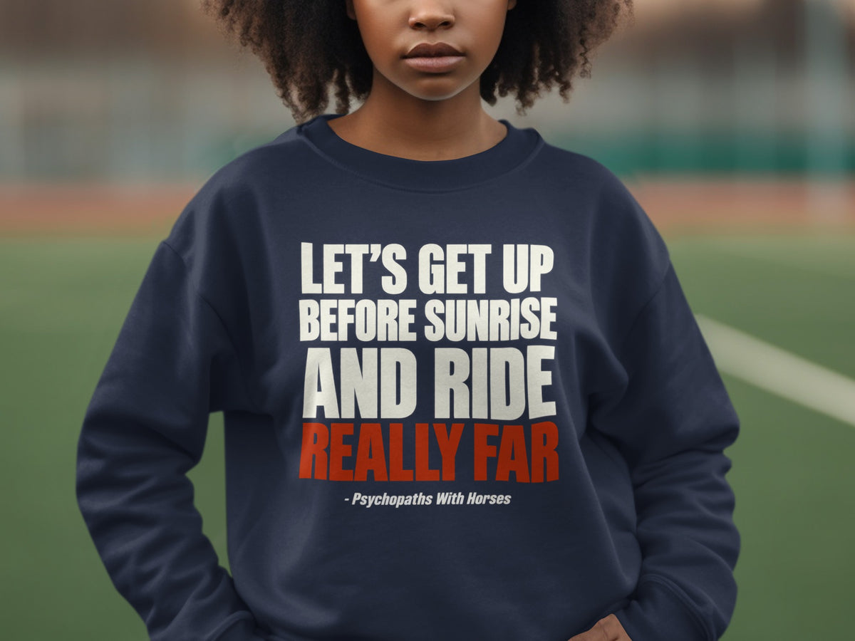 A person wearing a dark blue crewneck sweatshirt with white and red text stating, "Let's Get Up Before Sunrise And Ride Really Far - Psychopaths With Horses."