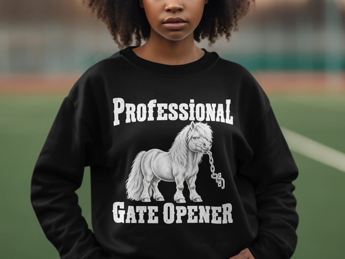 A person wears a black sweatshirt featuring a graphic of a miniature horse chewing a chain, with the text Professional Gate Opener.
