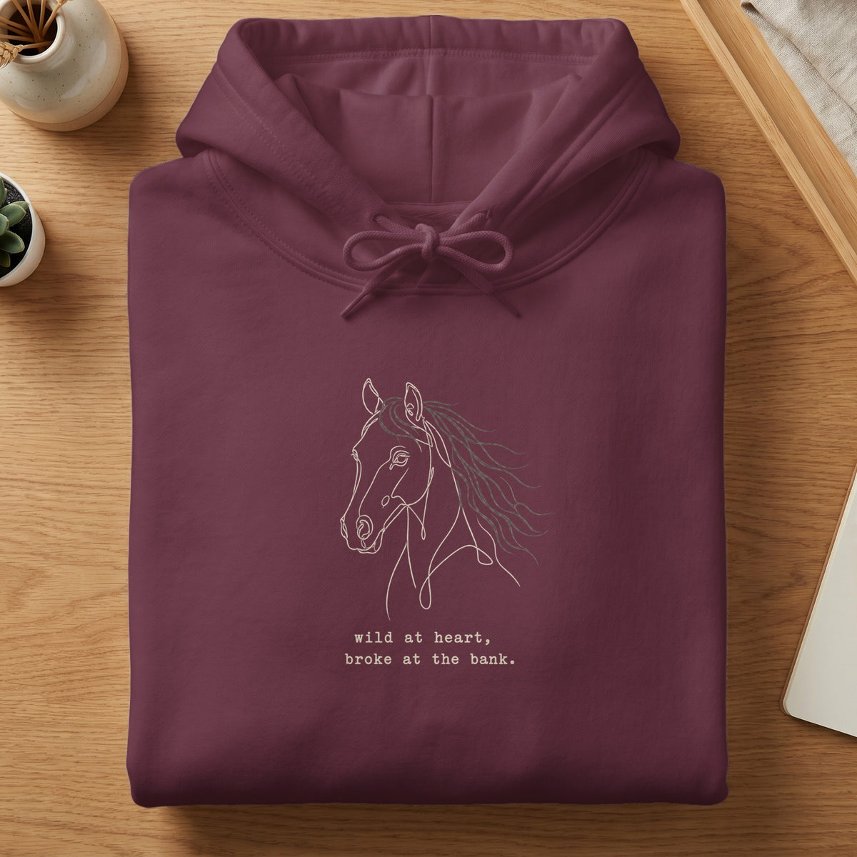 Maroon hoodie with a line drawing of a horse and the text "wild at heart, broke at the bank."