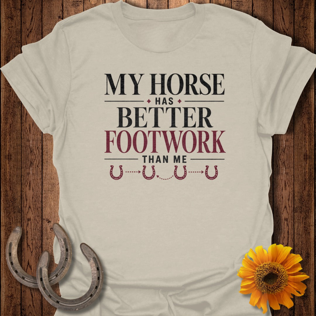 Light beige t-shirt with "My Horse Has Better Footwork Than Me" text and horseshoes.