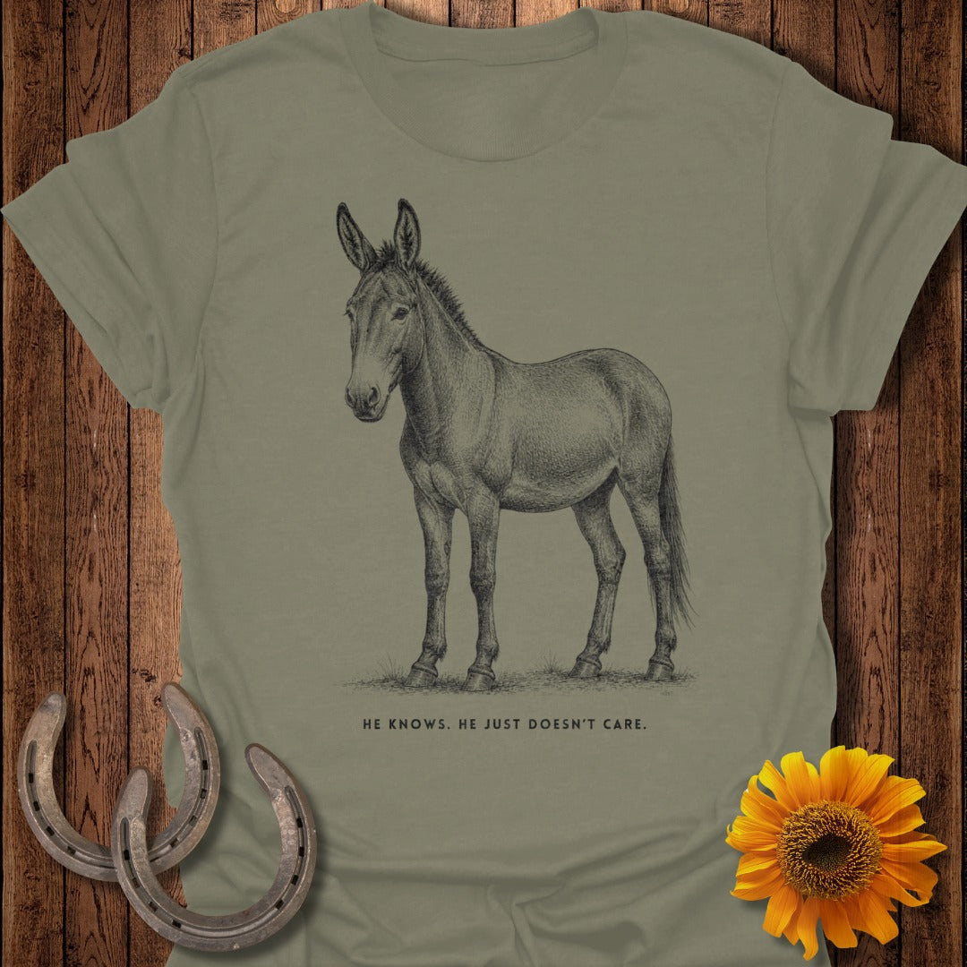 Line drawing of a mule on a khaki t-shirt with text below: "HE KNOWS. HE JUST DOESN'T CARE."