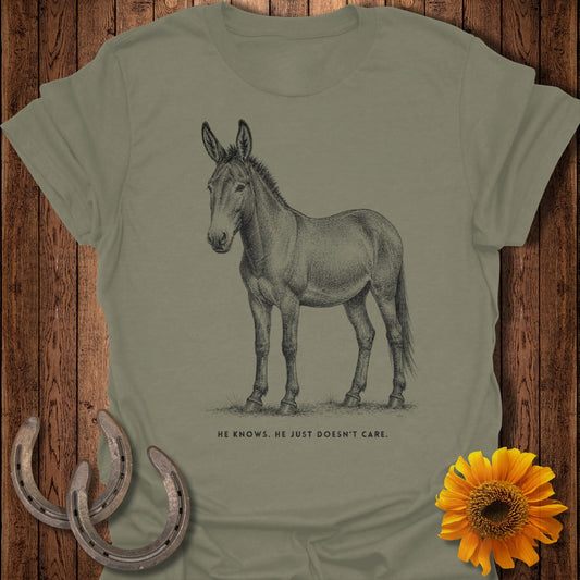 Line drawing of a mule on a khaki t-shirt with text below: "HE KNOWS. HE JUST DOESN'T CARE."
