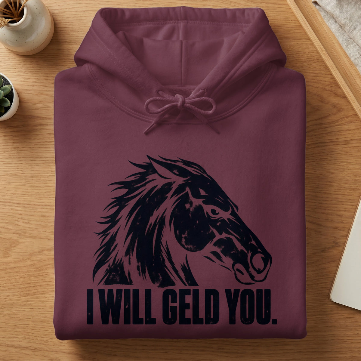 A folded maroon hoodie with a black horse graphic and text reading I WILL GELD YOU.