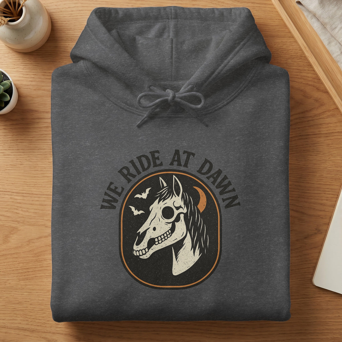 Dark gray hoodie with a graphic of a horse skull and text "WE RIDE AT DAWN".