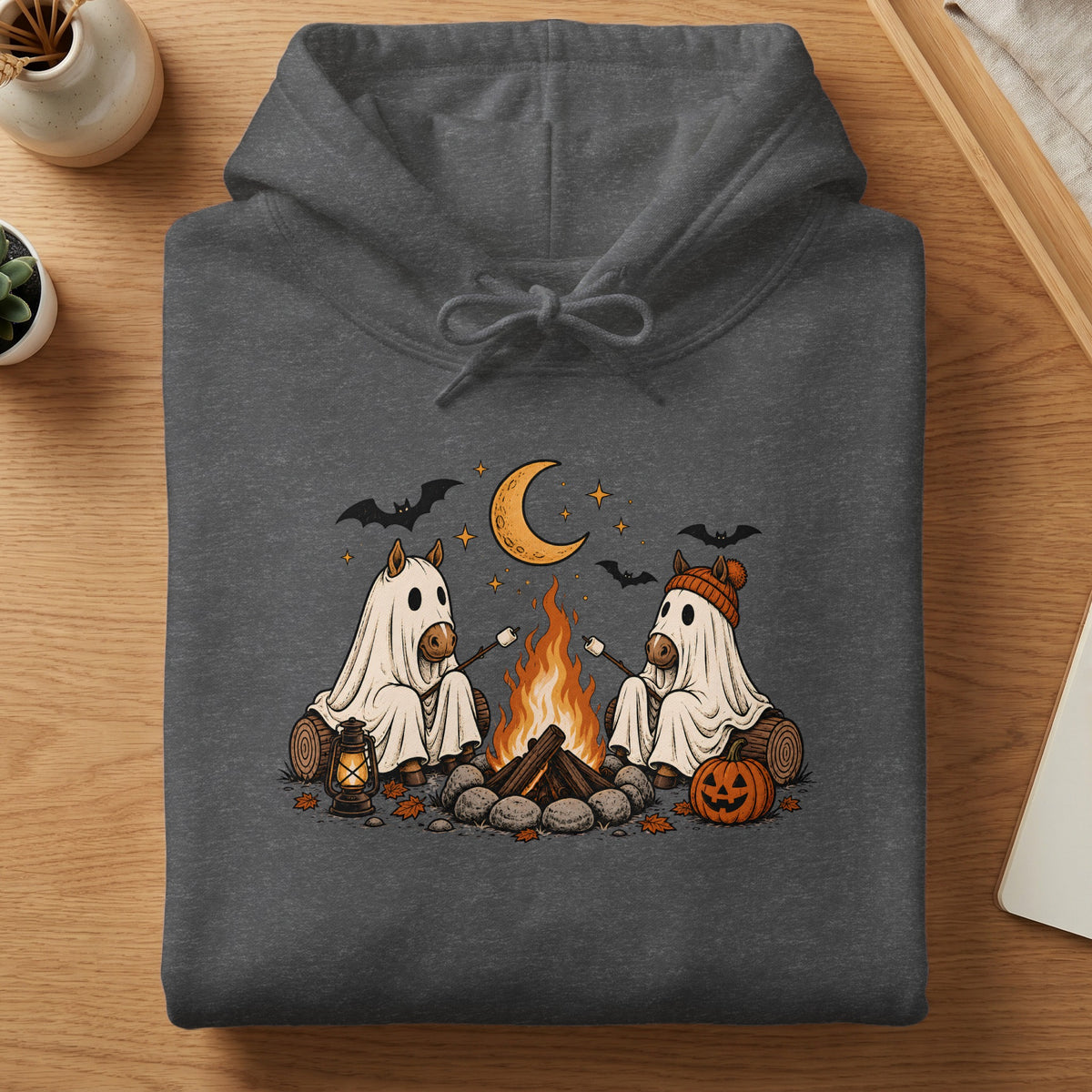Two horses in ghost costumes roast marshmallows by a campfire under a crescent moon.