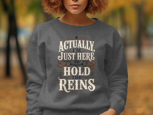 Dark grey sweatshirt with "Actually I'm Just Here To Hold The Reins" text and horse bit graphic.