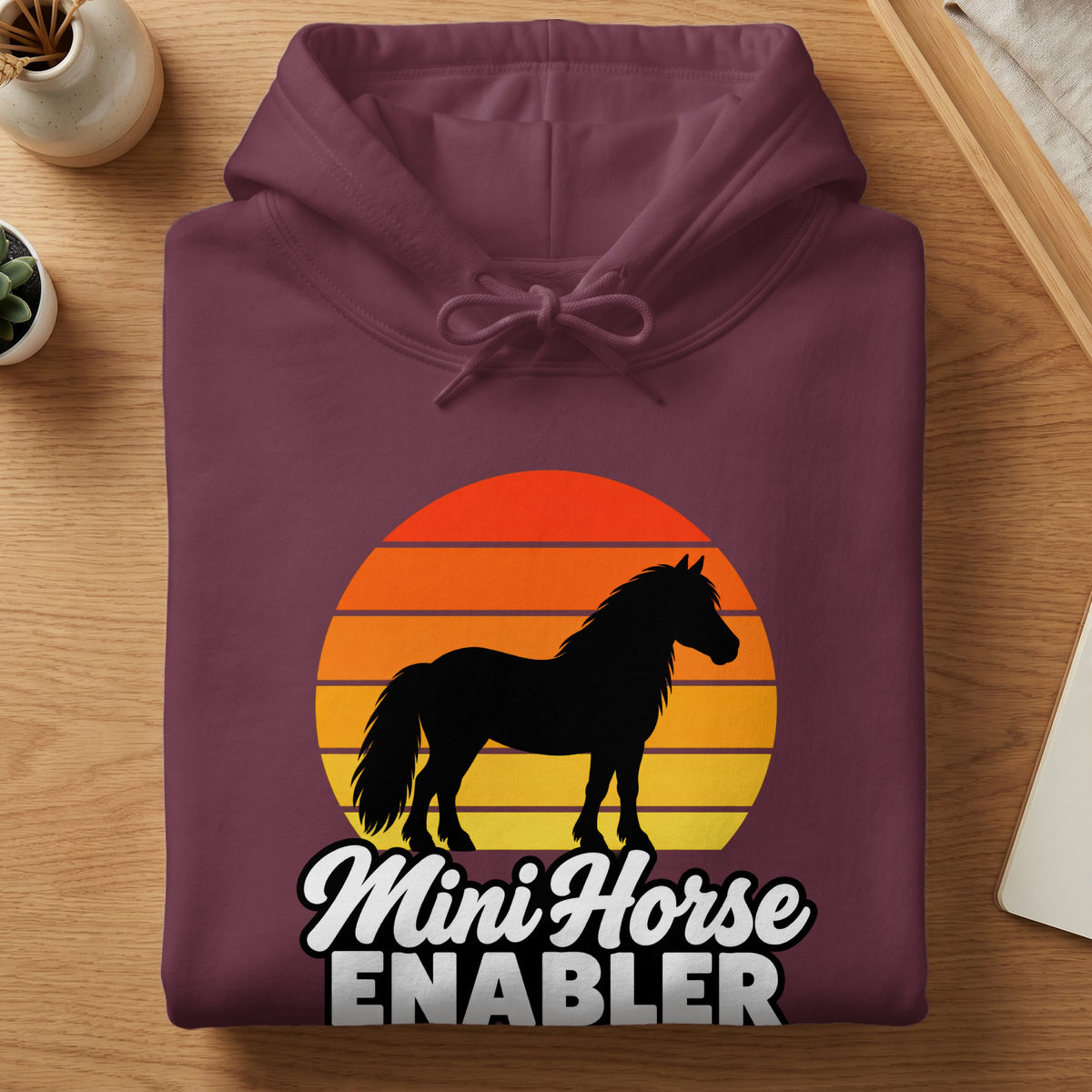 Folded dark purple hoodie featuring a graphic of a horse silhouette over a sunset and the text Mini Horse ENABLER.