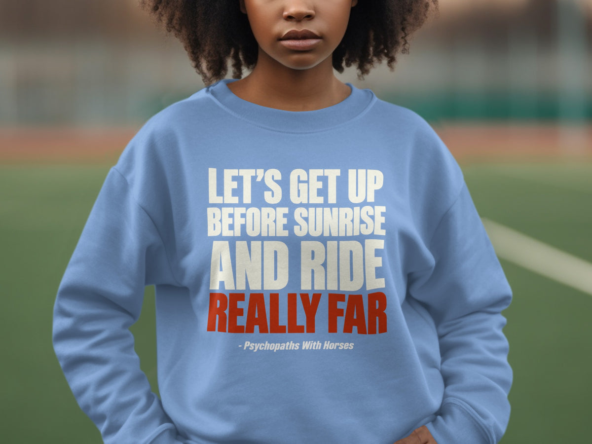 A person wearing a light blue crewneck sweatshirt with white and red text stating, Let's get up before sunrise and ride really far.
