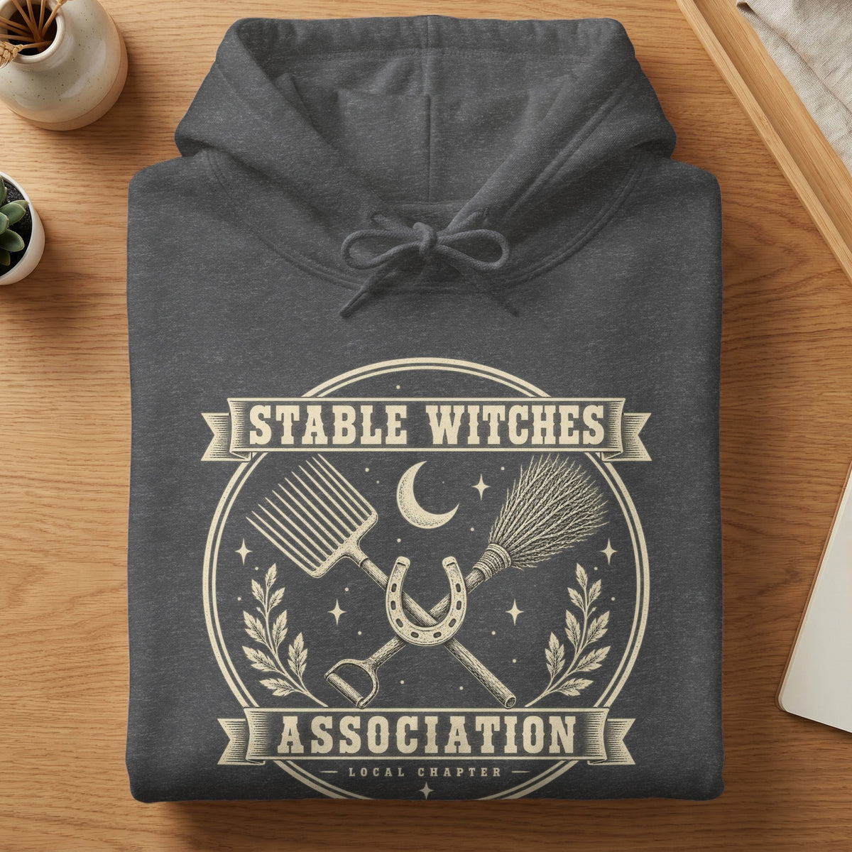 Dark grey hoodie with "Stable Witches Association Local Chapter" text and witchy stable imagery.