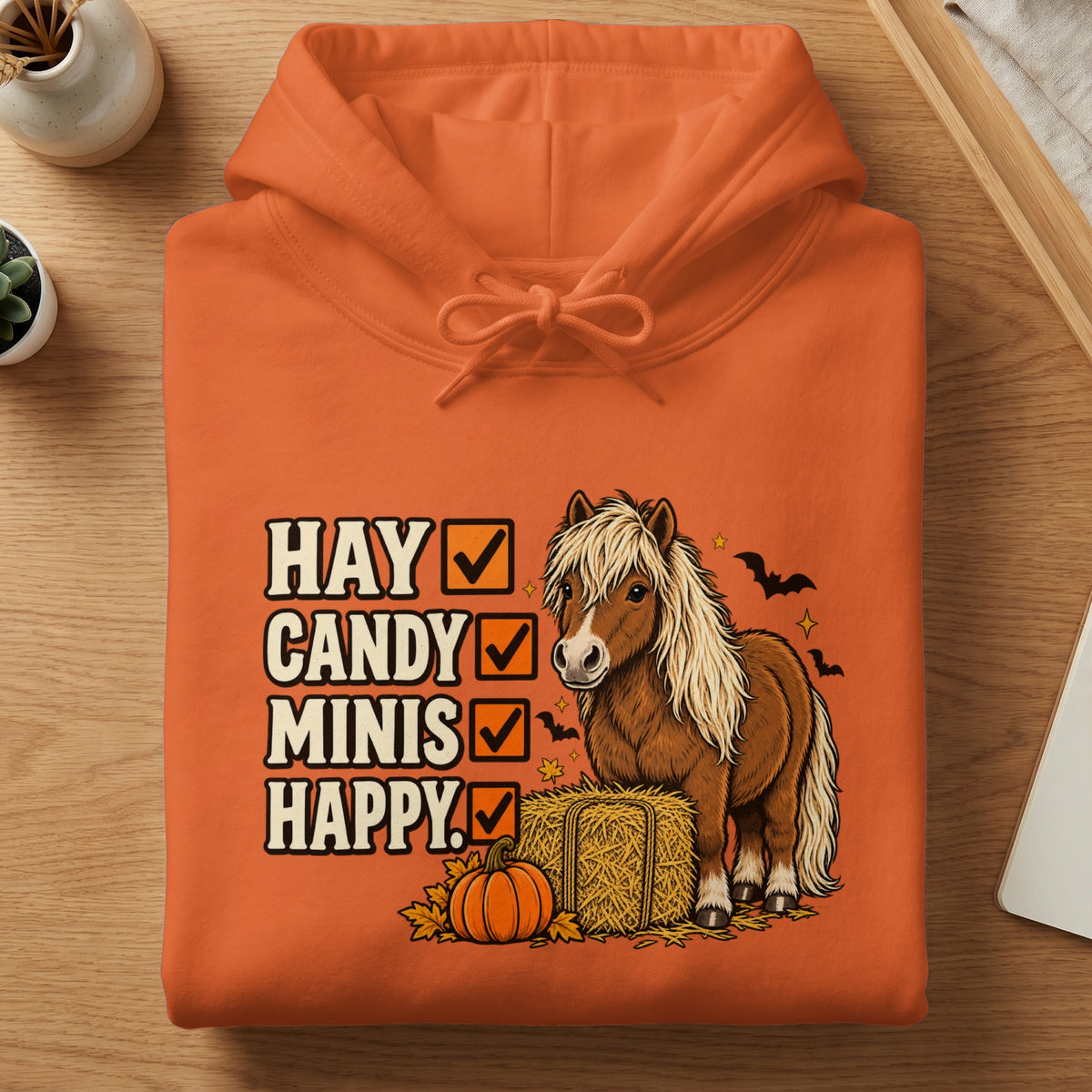 An orange hoodie printed with a pony, a hay bale, a pumpkin, and the text Hay, Candy, Minis, Happy.