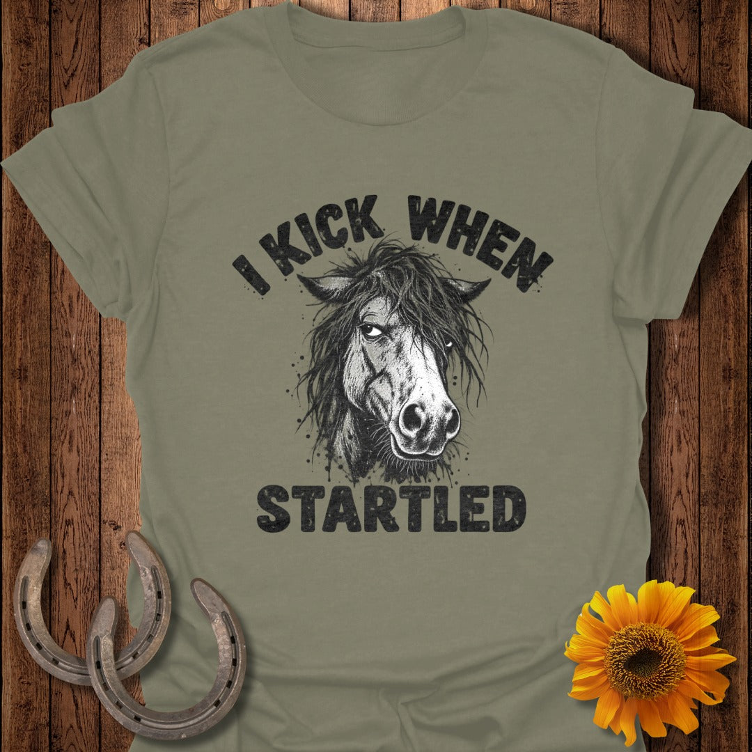An olive green t-shirt featuring a sketch of a horse head and the text I KICK WHEN STARTLED.