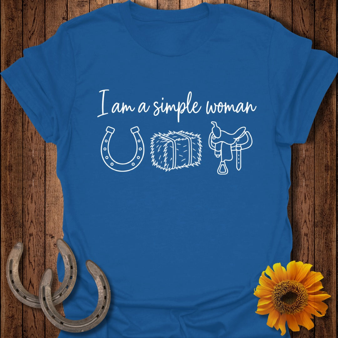 A royal blue t-shirt printed with the text I am a simple woman alongside white graphics of a horseshoe, a hay bale, and a saddle.