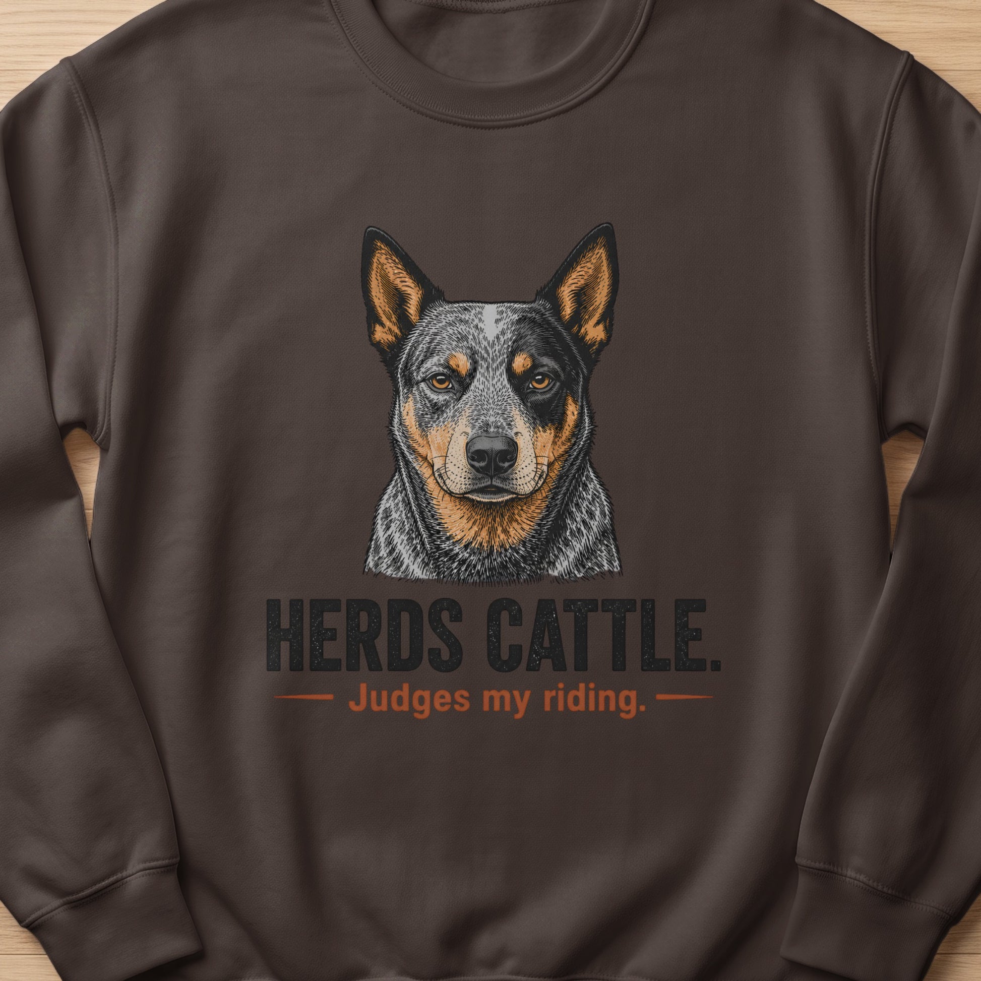 Brown sweatshirt with a drawing of an Australian Cattle Dog and text "Herds Cattle. Judges my riding."