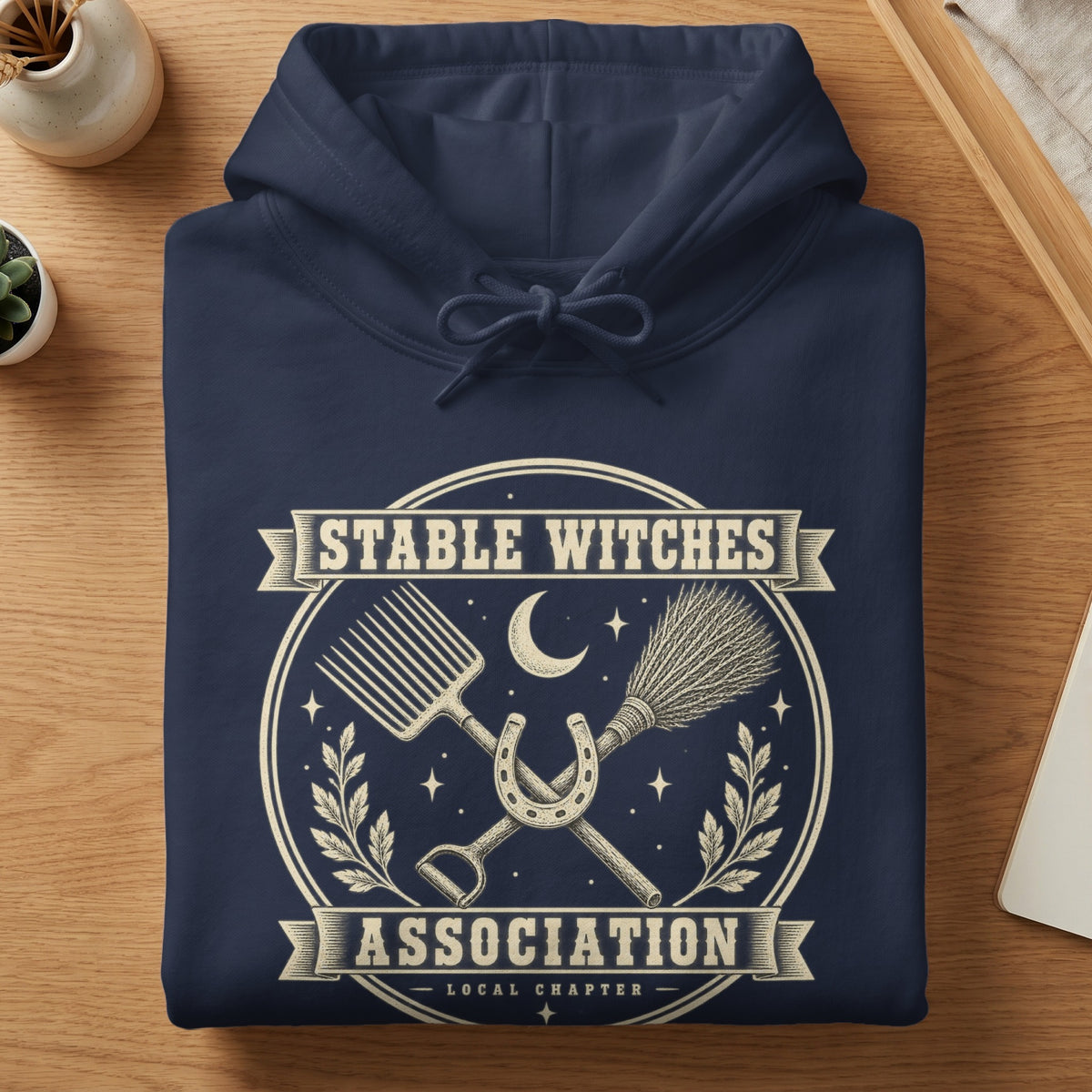 Navy hoodie with "Stable Witches Association Local Chapter" graphic featuring a horseshoe, broom, and pitchfork.