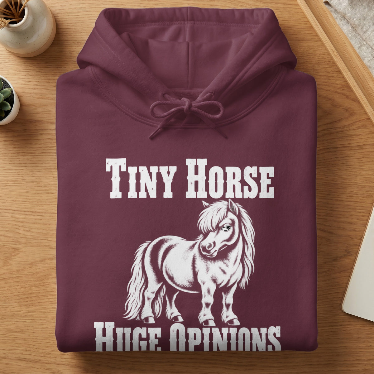 Folded maroon hoodie featuring white text reading Tiny Horse Huge Opinions with a graphic of a pony.