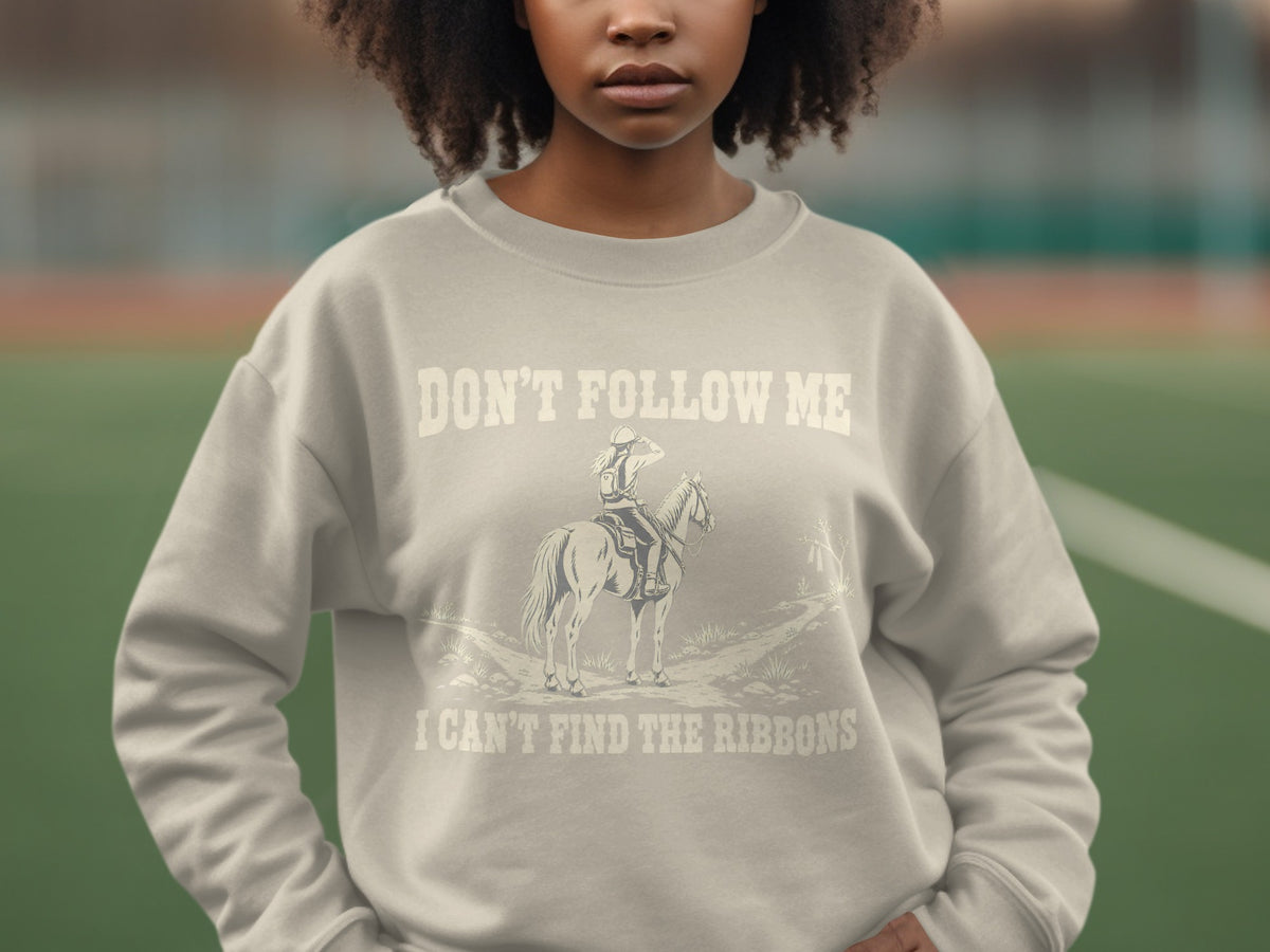 A person wears a beige sweatshirt featuring text and a graphic of a horse and rider.
