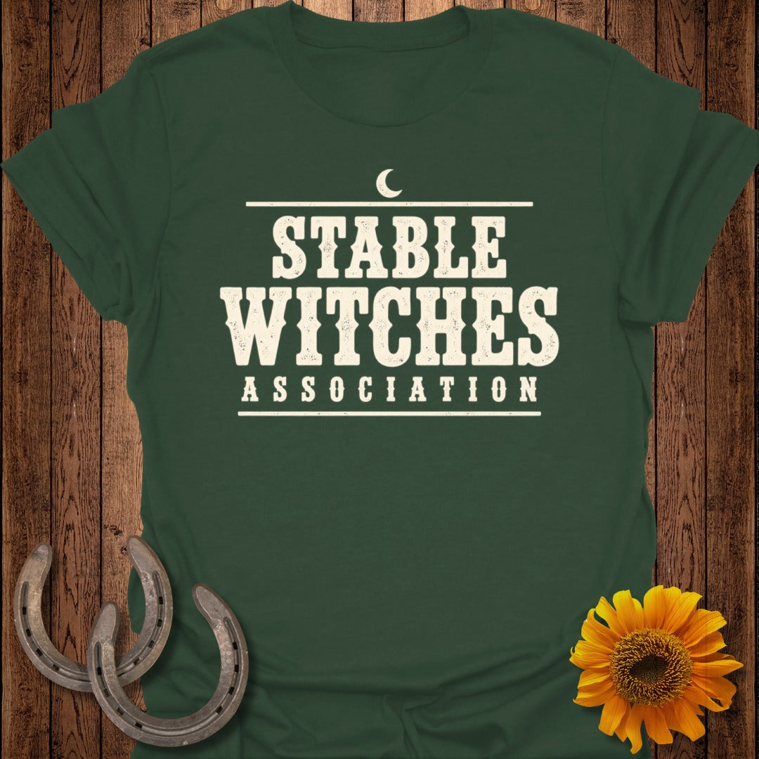 Dark green t-shirt with "Stable Witches Association" text, horseshoes, and sunflower.