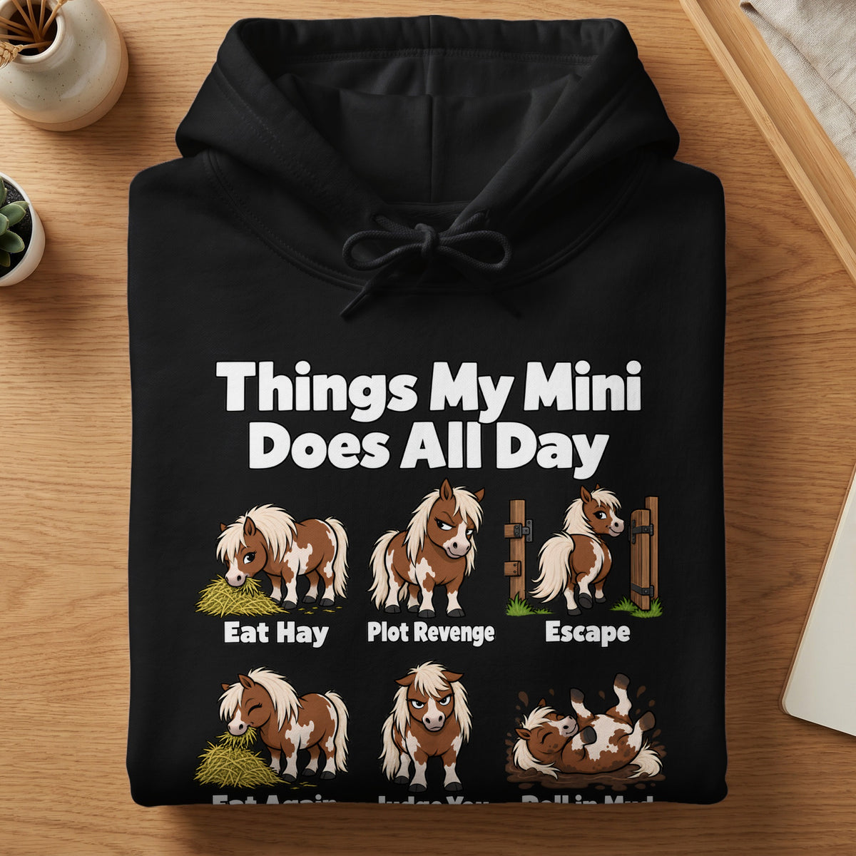 A folded black hoodie featuring a graphic and text about a mini horse's daily routine.