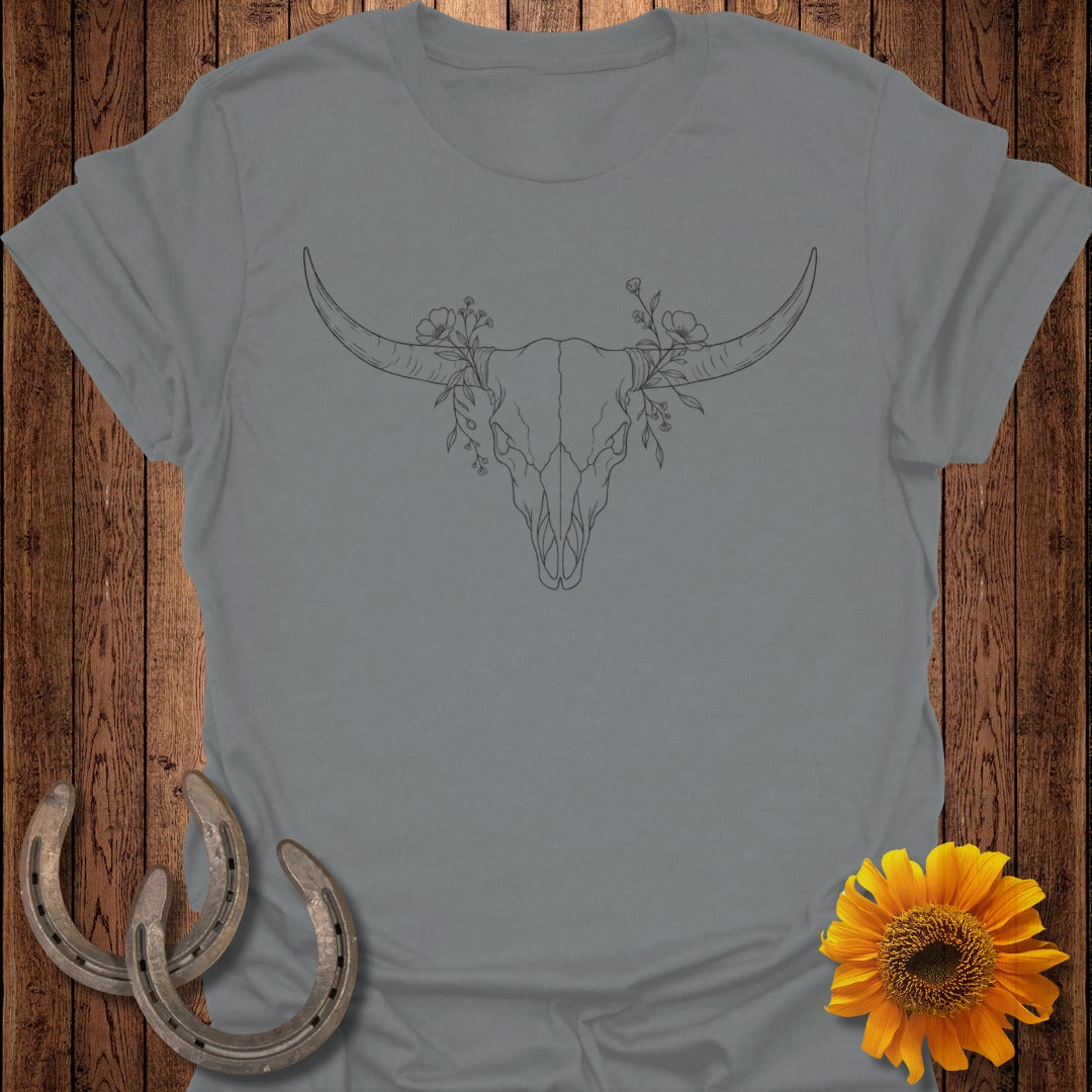 Gray t-shirt with a line drawing of a bull skull with flowers on rustic wood background.