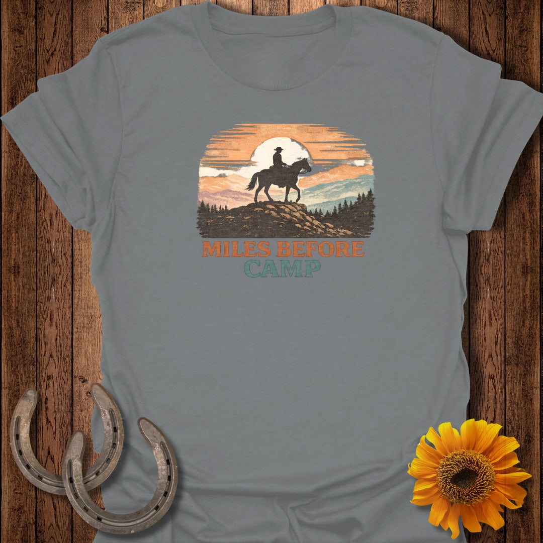 Grey t-shirt graphic with a silhouette of a rider on a horse on a hill, text reads "MILES BEFORE CAMP".