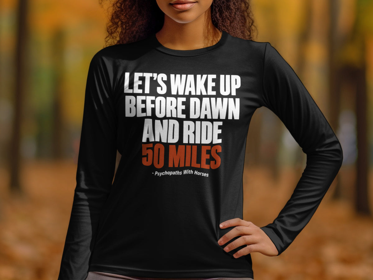 A person wearing a black long-sleeve shirt with white and orange text that reads "LET'S WAKE UP BEFORE DAWN AND RIDE 50 MILES - Psychopaths With Horses".