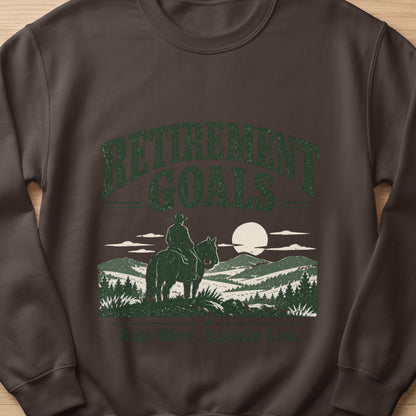 Brown sweatshirt with "Retirement Goals" and a cowboy on a horse at sunset graphic.