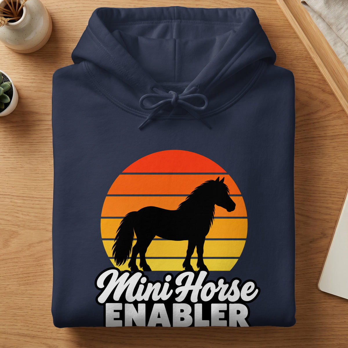 A folded navy blue hoodie with a sunset graphic, silhouetted horse, and the text Mini Horse Enabler.