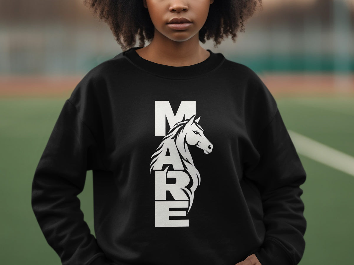 A person with dark curly hair wears a black crewneck sweatshirt featuring a vertical white graphic that reads MARE, with a horse's head integrated into the letters.