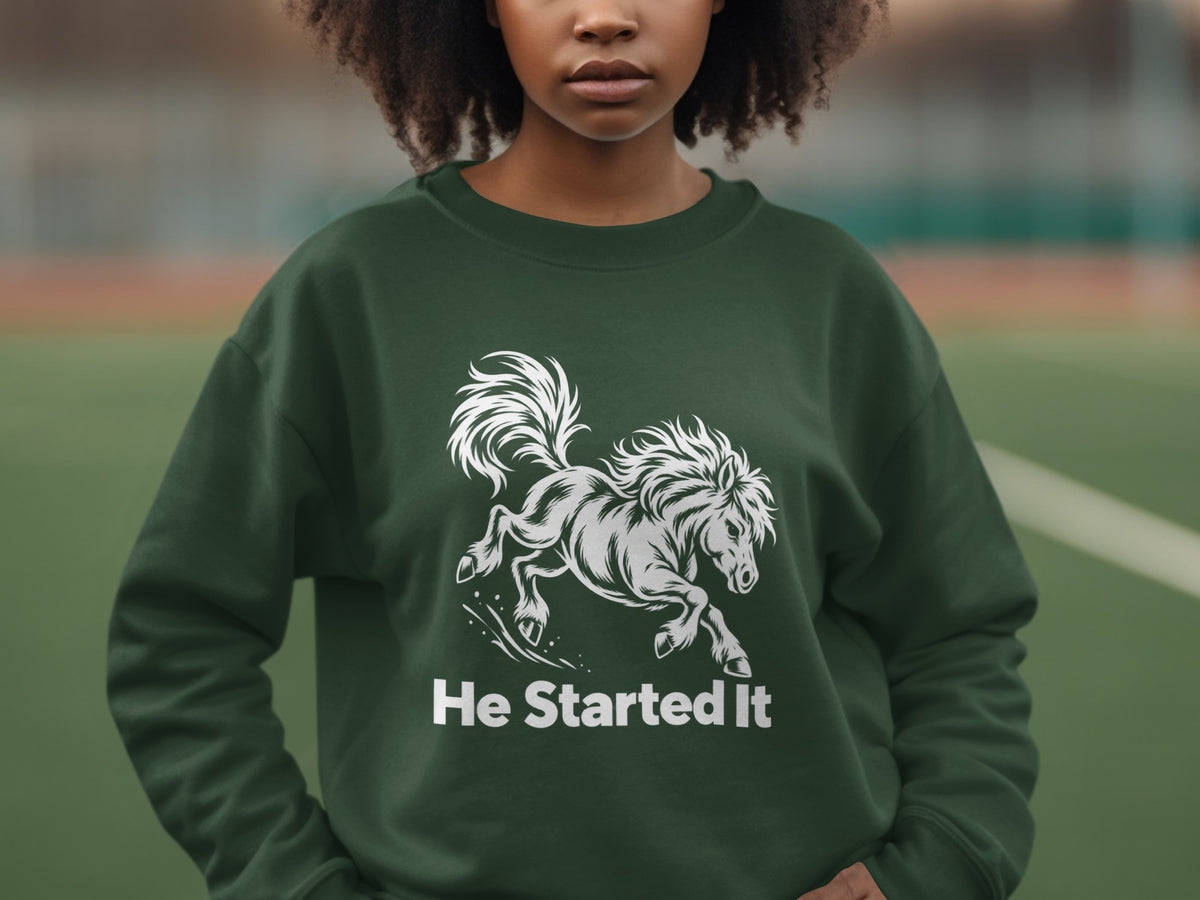 A person wears a dark green crewneck sweatshirt featuring a white graphic of a galloping horse with the text He Started It underneath.