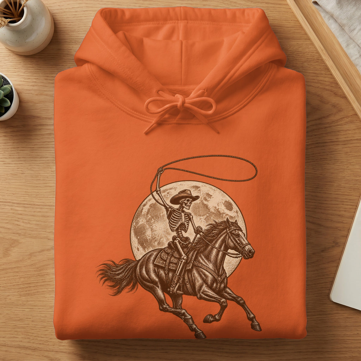 Orange hoodie with skeleton cowboy riding horse and moon graphic.