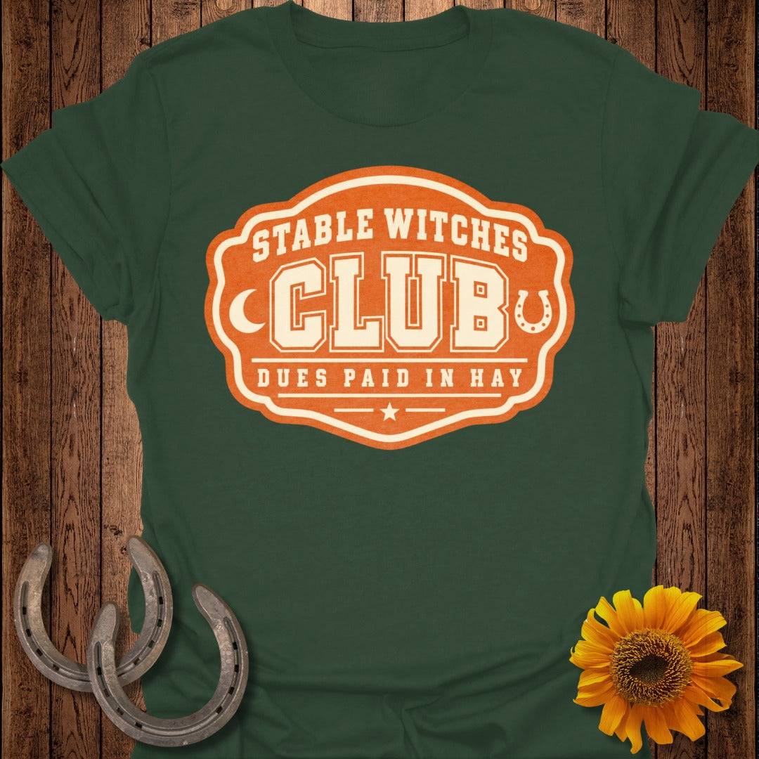 Green t-shirt with orange and cream "Stable Witches Club" graphic.