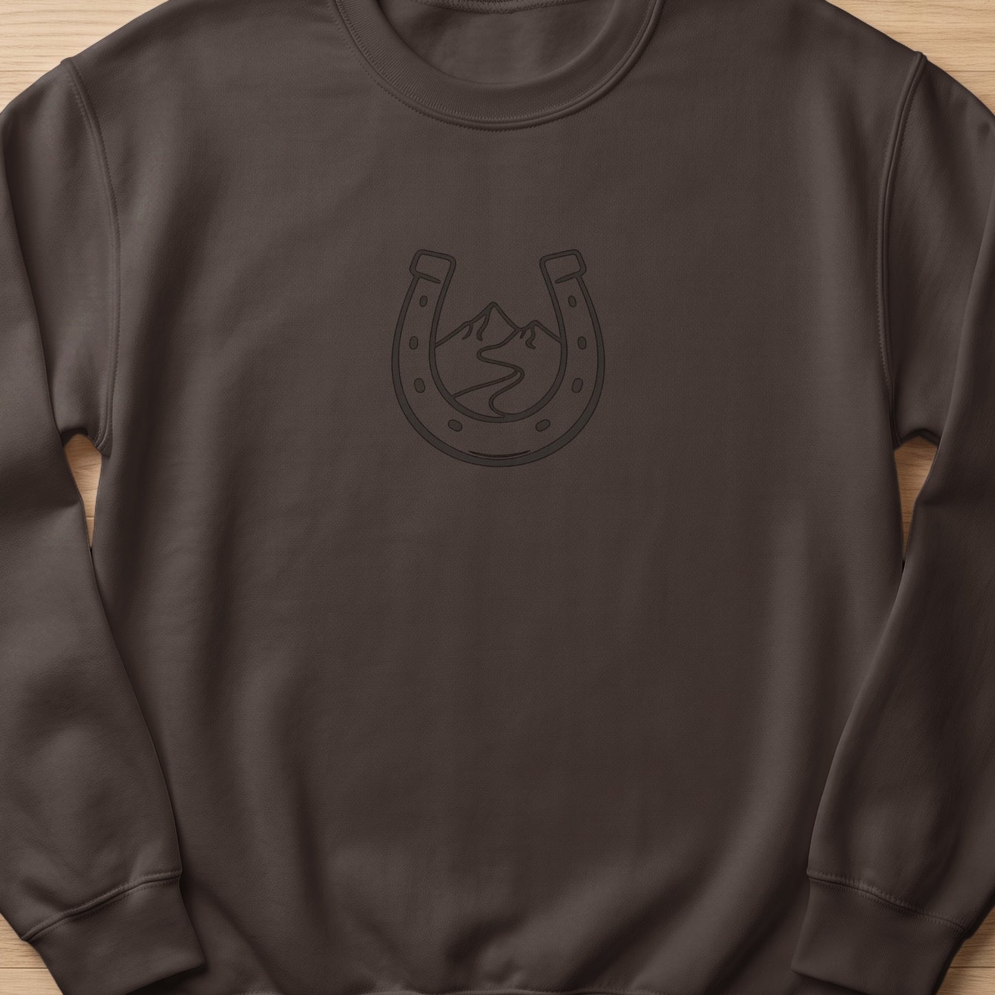 Brown sweatshirt with a horseshoe outline containing mountains and a winding road.