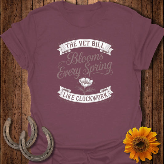 Burgundy t-shirt with text "The Vet Bill Blooms Every Spring Like Clockwork" and a flower.
