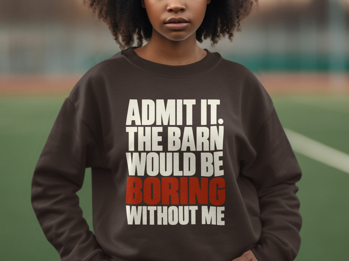 A person wearing a dark brown crewneck sweatshirt featuring white and red text reading ADMIT IT. THE BARN WOULD BE BORING WITHOUT ME.
