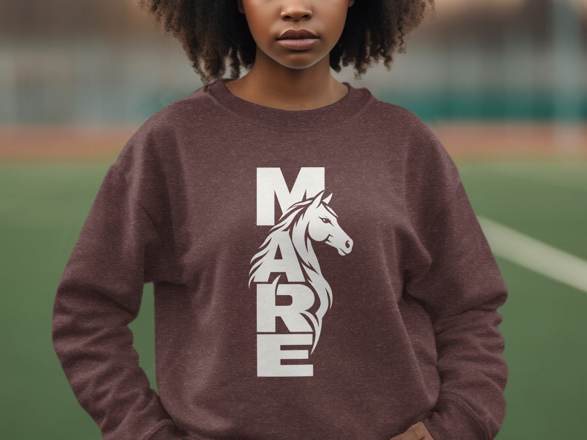 A person wearing a brown sweatshirt with white graphic text spelling MARE and a horse head.